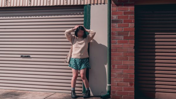 East Asian woman in a green sundress and cream sweater stands in front of a garage door with matching green gutters