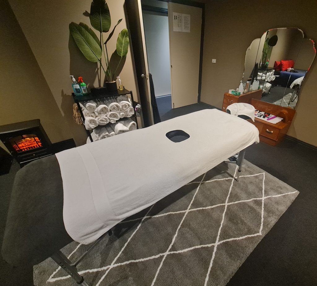 A milking massage table placed next to some white towels and massage oil