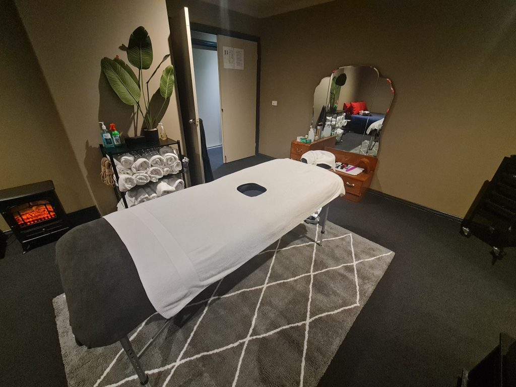 Milking massage table on a grey carpet in front of a large mirror.